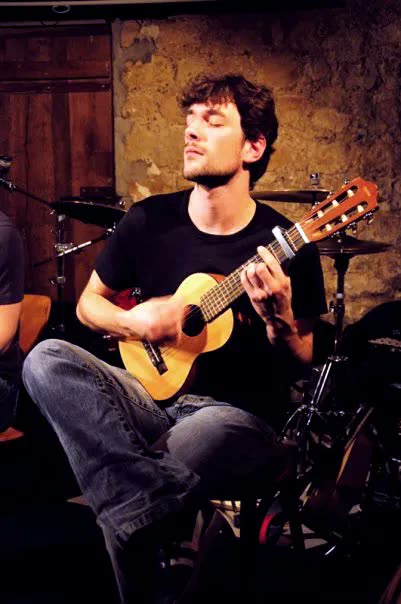 Löhstana David seated, playing a small nylon-string guitar