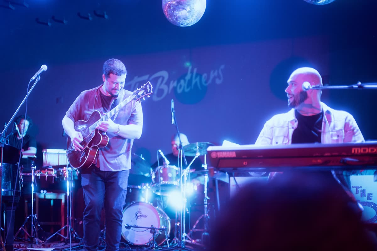 Guitar and keys on stage in blue light, the two players looking at each other