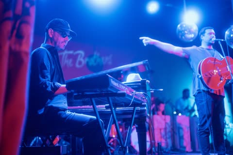 A guitarist pointing across the stage toward the keyboard player